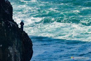 Pescador de la fortaleza de Sagres en uno de los salientes del acantilado. Mas o menos a media pared entre el nivel del mar y la parte superior del acantilado, un pescador se prepara para lazar la caña.